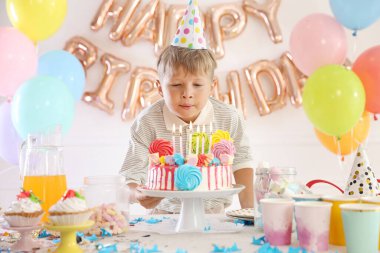 Doğum günü kutlaması. Şenlikli bir odada pasta masasında mumları üfleyen sevimli küçük çocuk.