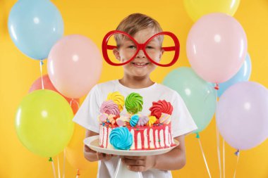 Doğum günü kutlaması. Tatlı ve turuncu arka planda balonları olan tatlı bir çocuk.