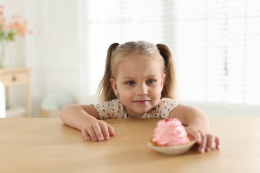 Şirin küçük kız ahşap masada lezzetli bir tatlıya uzanıyor.