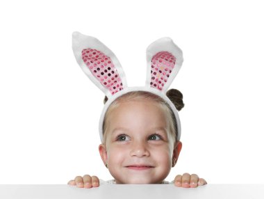 Tavşan kulaklı meraklı küçük kız beyaz arka planda masanın üstünden bakıyor.