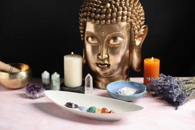 Çakra değerli taşları, tütsü, mumlar ve açık pembe masada Buda figürü.