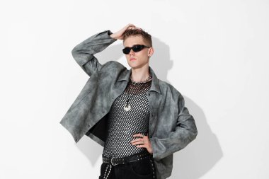 Beyaz arka planda şık ceket ve güneş gözlüğü takan yakışıklı bir genç.