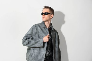 Beyaz arka planda şık ceket ve güneş gözlüğü takan yakışıklı bir genç.