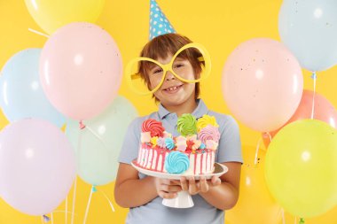 Doğum günü kutlaması. Tatlı ve turuncu arka planda balonları olan tatlı bir çocuk.