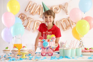 Doğum günü kutlaması. Masadaki tatlı küçük çocuk lezzetli pastayla ve çeşitli ziyafetlerle süslenmiş odada.