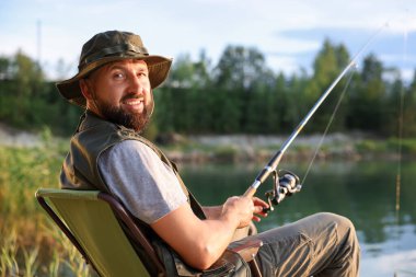 Yazın sandalyede oturan ve göl kenarında balık tutan oltalı balıkçı.