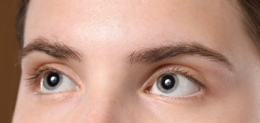 Kahverengi arka planda güzel kaşları olan genç bir kadın, yakın plan.