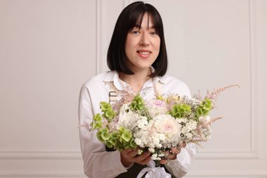 Beyaz duvarın yanında güzel çiçek buketi olan bir çiçekçi.