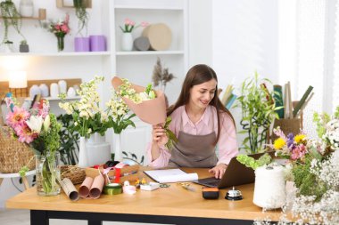 Dükkandaki tahta masada dizüstü bilgisayarla çalışan profesyonel bir çiçekçi.