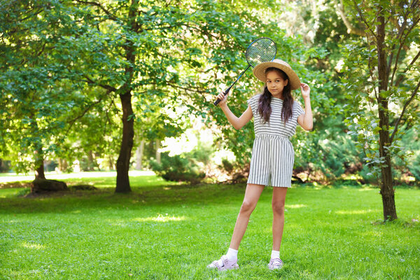 Милая маленькая девочка в шляпе с бадминтонной ракеткой в парке. Пространство для текста