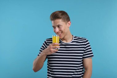 Açık mavi arka planda bir bardak portakal suyu olan mutlu bir adam. Tazeleyici içecek.