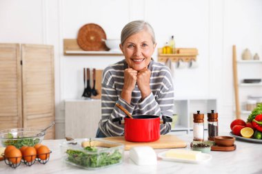 Üst düzey kadın mutfaktaki beyaz mermer masada yemek pişiriyor.