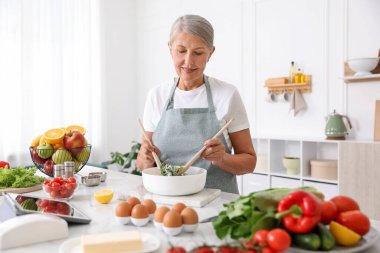 Üst düzey kadın mutfaktaki beyaz mermer masada salata pişiriyor.