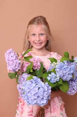 Bej arka planda hortensiya çiçekleri olan gülümseyen küçük bir kızın portresi