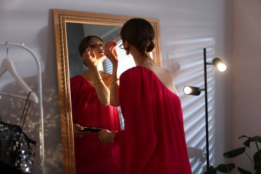 Güzel bir kadın aynanın yanında hazırlanırken makyaj yapıyor.