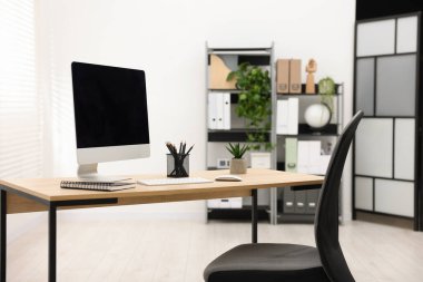 Ofisteki ahşap masa üzerinde modern bilgisayarı ve kırtasiyesi olan şık bir iş yeri.