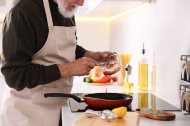 Mutfaktaki mutfağın tepesinde yemek pişiren yaşlı adam, yakın plan.