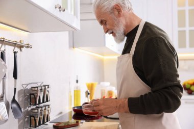 Mutfakta tezgahta yaşlı bir adam yemek pişiriyor.