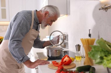 Mutfaktaki mutfağın tepesinde yaşlı bir adam yemek pişiriyor.