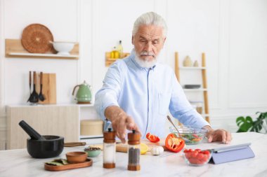 Mutfaktaki beyaz mermer masada yaşlı bir adam yemek pişiriyor.