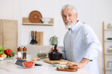 Mutfaktaki beyaz mermer masada yaşlı bir adam yemek pişiriyor.