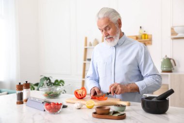 Mutfaktaki beyaz mermer masada yaşlı bir adam yemek pişiriyor.