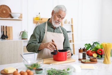 Mutfaktaki beyaz mermer masada yaşlı bir adam yemek pişiriyor.