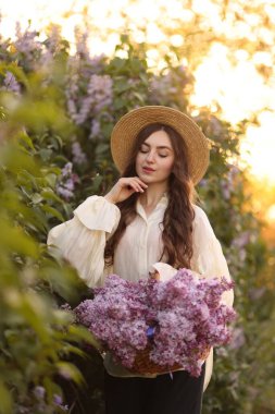 Güzel bir kadın, sabah çalıların yanında bir sepet leylak çiçeği taşıyor.