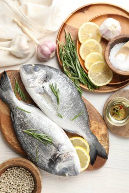 Taze çiğ dorado balığı, limon dilimleri, biberiye ve baharatlar beyaz ahşap masa, düz yatak. Organik deniz ürünleri