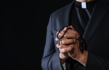 Siyah arka planda tespih çeken bir rahip, yakın plan. Metin için boşluk