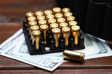 Ahşap masada bir sürü metal mermi, dolar ve cephane kemeri var.