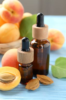 Yağ şişeleri, taze kayısılar ve çekirdekler açık mavi ahşap masa, yakın plan.