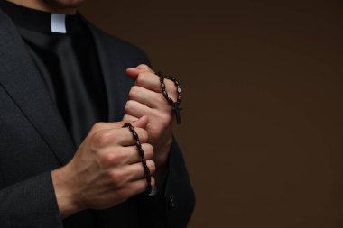 Kahverengi arka planda tespihi olan bir rahip, yakın plan. Metin için boşluk