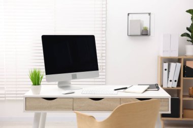 Ofisteki beyaz masa üzerinde modern bilgisayarı ve kırtasiyesi olan şık bir iş yeri.