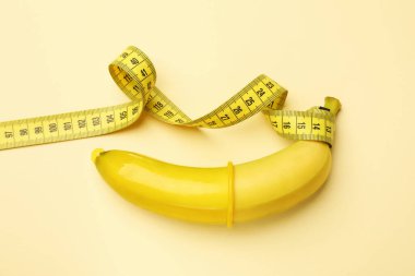 Seks eğitimi. Prezervatifli muz ve bej arka planda mezura, üst görünüm.