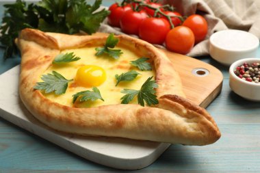Peynirli, yumurtalı, maydanozlu, domatesli ve baharatlı leziz khachapuri. Açık mavi ahşap masa, yakın plan.