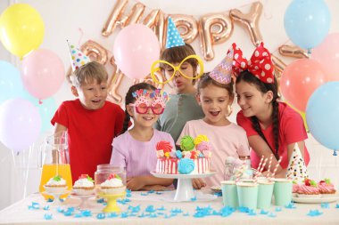 Doğum günü kutlaması. Masadaki çocuklar lezzetli pastalar ve dekoratif odalarda farklı şeyler yiyorlar.