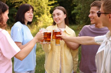 Bir grup mutlu arkadaş dışarıda bira bardaklarını tokuşturuyor.
