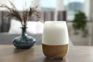 Modern aroma lambası ve vazodaki kuru bitkiler kapalı masa üzerinde.