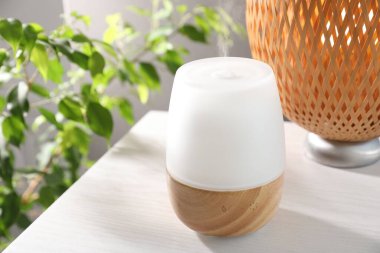 Beyaz ahşap masa üzerinde modern aroma lambası, yakın plan.