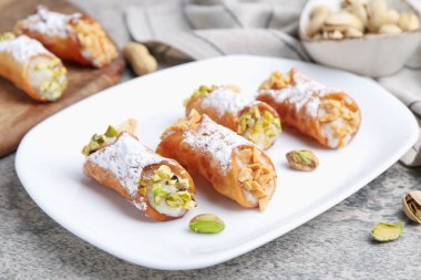 Ricotta peynirli, fıstıklı, şam fıstıklı ve pudra şekerli nefis cannoli. Gri desenli masa, yakın plan.