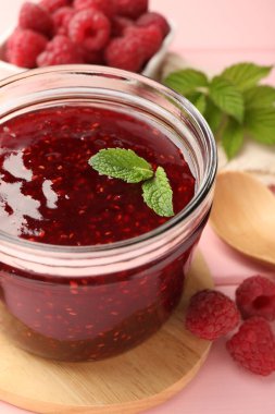 Cam kavanozda tatlı ahududu reçeli, pembe ahşap masada nane ve böğürtlen, yakın plan.