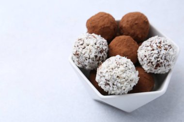 Beyaz masadaki kasede kakao tozu ve hindistan cevizi gevreği bulunan nefis ev yapımı şekerler, yakın plan. Metin için boşluk