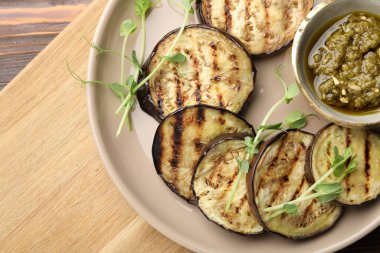 Soslu ızgara patlıcan dilimleri ve ahşap masada mikroyeşiller.