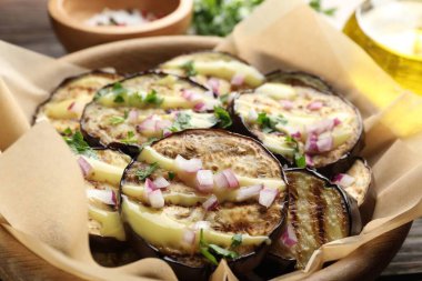 Ahşap masada servis edilen soslu, maydanozlu ve soğanlı ızgara patlıcan dilimleri.