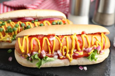 Gri masada soslu, marullu ve soğanlı lezzetli sosisliler, yakın plan.