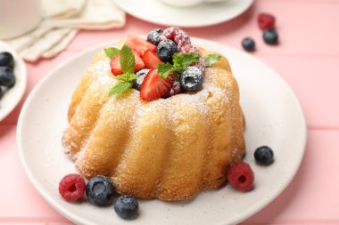 Pudra şekerli, böğürtlenli ve nane şekerli nefis kek, pembe ahşap masa, yakın plan.