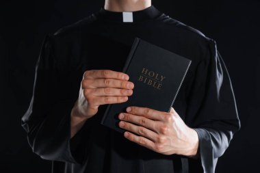 Siyah arka planda İncil 'i olan rahip, yakın plan.