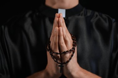 Siyah arka planda tespih çeken rahip, yakın plan.