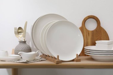 Temiz bulaşık takımı ve tahta kesme tahtası beyaz duvarın yanında.